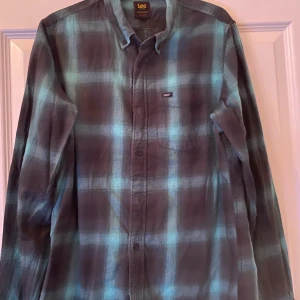 Rutig blå, svart, mörkgrön skjorta från Lee - Säljer en rutig långärmad skjorta från Lee i blått, mörkgrönt och svart. Skjortan har klassisk krage, knäppning framtill och en bröstficka med Lee-logga. Regular fit och riktigt skön bomullskänsla, perfekt för en avslappnad stil.