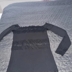 Svart spetsblus från Intimissimi - Säljer en svart blus från Intimissimi i storlek S. Blusen har långa ärmar och är dekorerad med breda spetsdetaljer över bröstet, midjan och ärmsluten. Offshoulder-modell med stretchigt material som sitter snyggt och bekvämt. Perfekt för dig som gillar romantisk stil. I väldigt fin skick I storlek S  