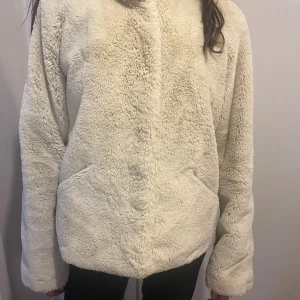 Vit teddyjacka från ONLY, storlek L - Mysig Höst/Vår teddyjacka från ONLY i storlek L. Jackan är vit och har en fluffig, mjuk yta med hög krage och två sidofickor. 