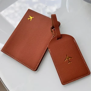 Brunt passfodral & bagagetagg  - Snyggt set med passfodral och bagagetagg i brunt skinnimitation, dekorerade med en guldfärgad flygplanssymbol. Passfodralet har plats för pass och kort, medan taggen har fönster för kontaktinfo. Perfekt för resor och ger din väska en clean look.🤎 Helt nytt