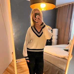 Vit stickad v-ringad tröja med marinblå detaljer - Säljer en vit stickad tröja från Primark med marinblå ränder vid v-ringningen, ärmsluten och midjan. Tröjan har en klassisk, sportig look och är långärmad med ribbade muddar. Perfekt för dig som gillar preppy stil!