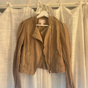 Brun jacka med dragkedja - Snygg brun jacka med asymmetrisk dragkedja och två fickor framtill. Jackan har en kortare passform och är tillverkad i ett mjukt bomullsmaterial. Perfekt för lager-på-lager och enkel att styla till olika outfits.