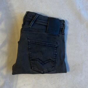 Replay Anbass Hyperflex svarta jeans - Svarta Replay Anbass Hyperflex jeans med klassisk femficksdesign och raka ben. Jeansen har snygga detaljer på bakfickorna och ett svart Replay-märke vid midjan. Stretchigt material för extra komfort och passform. Perfekt för dig som gillar stilrena och moderna jeans.