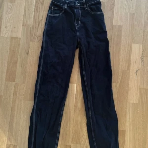 Svarta cargopants från Lindex - Svarta cargopants från Lindex med kontrasterande vita sömmar och flera fickor, inklusive bakfickor med dekorativa sömmar. Byxorna har rak passform och är tillverkade i bomull. Perfekta för en avslappnad och cool stil.