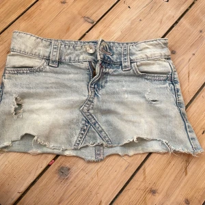 Ljusblå jeanskjol  - Säljer en kort ljusblå jeanskjol med slitna detaljer och rå kant. Kjolen har klassiska fickor fram och bak, bälteshällor och snygg broderad design på bakfickorna i rosa och grått. Perfekt för dig som gillar en edgy och avslappnad stil.