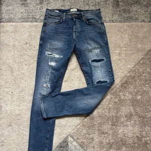 Jack & Jones slitna slim jeans blå - Blå jeans från Jack & Jones i modellen Glenn Slim Fit. Jeansen har slitna detaljer och hål på benen för en cool, avslappnad look. Klassisk femficksmodell med normal midja och smal passform. Tillverkade i mjukt denimtyg.