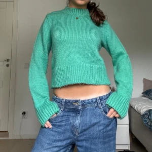 Grön stickad croppad tröja - Snygg grön stickad tröja med croppad passform och breda muddar. Tröjan har lång ärm och hög hals