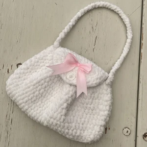 Virkad handväska - Vit virkad handväska med rosa rosett. Virkad med ett mjukt garn, ca 24 cm bred💕