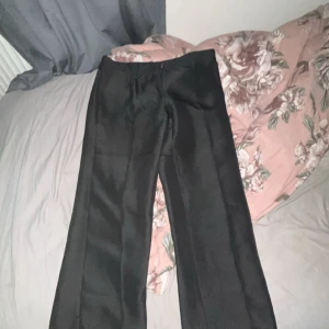 Svarta kostymbyxor från Nelly - Snygga svarta kostymbyxor från Nelly i klassisk rak modell. Byxorna har hög midja och vida ben, perfekta för en clean och stilren look. Materialet är slätt och ger en dressad känsla. Passar dig som gillar minimalistisk stil.