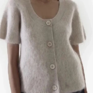 Beige stickad kofta från COS - Supermjuk och fluffig beige stickad kofta från COS med kort ärm och stora knappar framtill. Koftan har en rund, djup ringning och är tillverkad i en ullblandning som känns lyxig och cozy. Perfekt att slänga över en topp för en chill look. Inga defekter, nästan aldrig använd!❤️