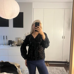 Svart blommig spetsblus med v-ringning - Jättefin blus med knappar framtill, den är i storlek L men är mer som en M/S
