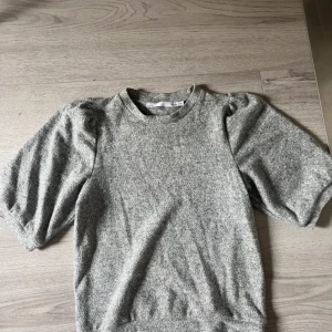 Grå puffärm tröja  - Säljer en grå tröja från H&M med puffade korta ärmar och rund hals. Tröjan har en mjuk och lite tjockare känsla, perfekt för dig som gillar enkel men trendig stil. Passar dig som vill ha något bekvämt och snyggt till vardags. Knappt använd 