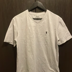 Ljus grå t-shirt från Polo Ralph Lauren - Ljus grå t-shirt från Polo Ralph Lauren med klassisk v-ringning och broderad logga på bröstet. Modellen är slim fit och har korta ärmar. Tillverkad i mjuk bomull som känns skön mot huden. Perfekt för en clean och stilren look.