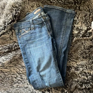 Blå bootcut jeans från See Thru Soul - Snygga blå jeans från See Thru Soul med bootcut-modell och coola broderade detaljer på bakfickorna. Klassisk femficksdesign, normal passform och i mjukt jeanstyg. Perfekta för dig som gillar en avslappnad men trendig look.