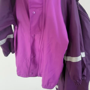 Lila regnjacka med reflexdetaljer - Snygg regnjacka i två olika lila nyanser med reflexband på ärmarna.