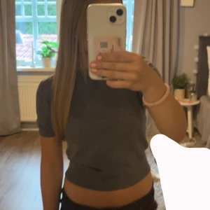 Grå croppad topp från H&M Divided - Grå croppad topp från H&M Divided med korta ärmar och rund halsringning. Toppens material är mjukt och ribbat, vilket ger en skön känsla och snygg passform. Perfekt till jeans eller kjol för en chill look.