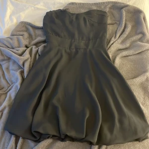 Svart axelbandslös klänning från ASOS - Supersnygg svart axelbandslös kortklänning från ASOS med markerad midja (saknar band) och lätt puffig kjol. Klänningen har dragkedja i sidan. 