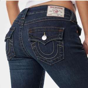 True Religion mörkblå bootcut jeans - Mörkblå jeans från True Religion med ikoniska kontrastsömmar och stora bakfickor med lock och silverknappar. Låg midja och bootcut. Har sytt upp jeansen med maskin så att de passar någon som är runt 165cm. Säljer då jag har för många jeans💕