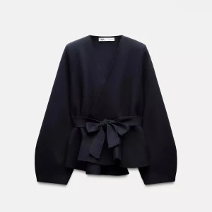 Svart omlottkofta med knyt från Zara - Snygg svart omlottkofta från Zara med breda långa ärmar och ett stort knytband i midjan. Koftan har v-ringad hals och är tillverkad i ett mjukt stickat material som ger en chill och stilren vibe. Perfekt för lager-på-lager och att dressa upp din outfit.