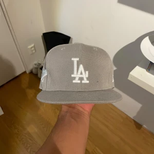 Grå LA Dodgers keps New Era 59FIFTY - Har tre till färger som jag säljer då jag råka köpa fel stolek. Helt nya. Snygg grå LA Dodgers keps från New Era 59FIFTY-serien. Klassisk modell med platt skärm, broderad LA-logga framtill och World Series 1981-märke på sidan. Tillverkad i 100% polyester och har en clean look som passar streetwear.