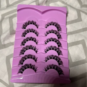 6-pack dramatiska lösögonfransar - Säljer ett 6-pack svarta lösögonfransar med volym och fluffig look. Fransarna är täta och har en böjd form för en intensiv blick. De kommer i en lila plastförpackning. Perfekt för dig som vill ha en extra wow-effekt till din makeup.