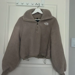 Beige fleece hoodie från The North Face - Supermjuk och oversized beige fleece hoodie från The North Face. Tröjan har halv dragkedja, hög krage och snörning i midjan. Långa ärmar med ribbade muddar och förstärkta partier på armbågarna. Supermysig inför höst och vinter. Enbart använd en gång.                            !Pris kan diskuteras!