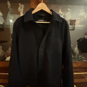 Svart overshirt från J.Lindeberg - Stilren svart overshirt från J.Lindeberg med klassisk krage, bröstficka och knäppning framtill. Jackan har lång ärm och är tillverkad i ett mjukt material som passar perfekt för lager-på-lager. Enkel och clean look som funkar till det mesta. Nypris cirka 2000kr, använd sparsamt! 