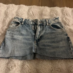 Blå jeanskjol från Bershka 90's - Säljer en blå jeanskjol från Bershka i 90-talsstil. Kjolen är kort med rå, fransig fåll och slitna detaljer både fram och bak. Klassisk femficksmodell med bälteshällor och dragkedja. 