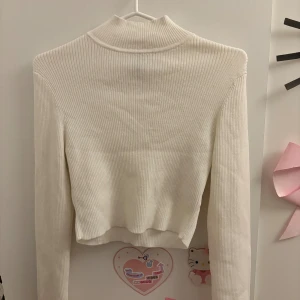 Vit ribbad polotröja från H&M - Säljer en vit ribbad polotröja från H&M i storlek M. Tröjan har lång ärm, croppad passform och är tillverkad i mjuk, stretchig bomullsmix. Perfekt för lager-på-lager och har en clean, stilren look med hög krage.