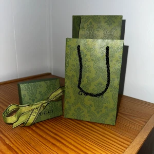 Silverfärgat armband från Gucci - Säljer ett snyggt armband från Gucci i silverfärgad metall med klassiska GG-loggor på flera av länkarna. Kommer i original ask, påse och presentpåse med Guccis gröna mönster. Perfekt accessoar för dig som gillar lyxiga detaljer.