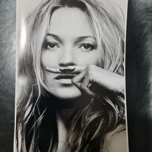 Affisch 21x30 Kate Moss - Bokens omslag visar ett konstnärligt svartvitt porträtt av en person med långt hår. Omslaget ger en modern och stilren känsla som kan tilltala unga vuxna och ungdomar. Mer information om titel och författare saknas på bilden.