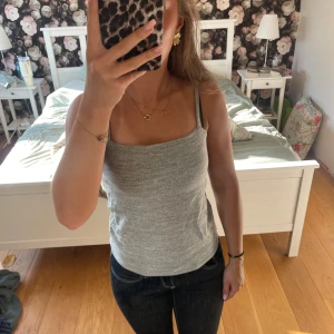 Grå ribbad linnetopp - Säljer en enkel och stilren grå linnetopp med smala axelband och rak halsringning. Toppen är ribbad och har en tight passform som sitter snyggt mot kroppen. Perfekt att matcha med jeans eller kjol för en clean look.