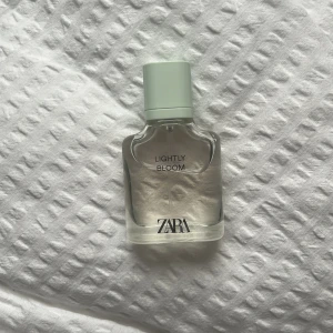 ZARA Lightly Bloom parfym - Fräsch parfym från ZARA med namnet Lightly Bloom. Flaskan är genomskinlig med en ljusgrön kork och minimalistisk design. Perfekt för dig som gillar lätta och blommiga dofter. Flaskan är i glas och har raka, stilrena linjer.