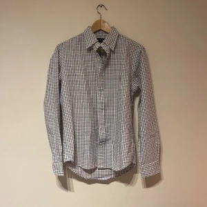 Rutig skjorta från Polo Ralph Lauren - Säljer en klassisk rutig skjorta från Polo Ralph Lauren i vitt med blå och svarta rutor. Skjortan har lång ärm, knappar framtill och broderad logga på bröstet. Custom fit-modell i mjuk bomull, perfekt till jeans eller chinos.