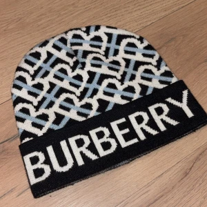 Burberry stickad mössa med logga - Snygg stickad mössa från Burberry med grafiskt mönster i svart, vitt och ljusblått. Stor vikt kant med tydlig BURBERRY-logga framtill. Klassisk passform och mjukt material som håller dig varm och stilsäker.