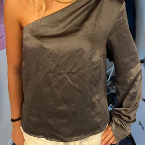 Grå silkeslen oneshoulder-top - Snygg grå topp i silkesliknande material med en axel bar och en lång ärm.🥰