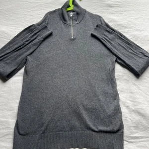 Grå half zip stickad tröja - Snygg grå stickad tröja med half zip och hög krage. Tröjan har ribbade muddar och långärmad design som ger en chill och stilren vibe. Perfekt för dig som gillar enkel men cool stil.