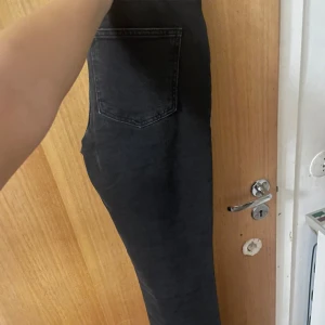 Svarta jeans med hög midja - Snygga svarta jeans med hög midja och klassisk bakficka. Jeansen har en tight passform och är perfekta för dig som gillar en stilren look. Materialet är stretchigt och bekvämt, vilket gör dem lätta att bära hela dagen.
