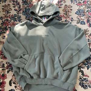 Grön hoodie från District Fortysix - Snygg grön hoodie från District Fortysix i storlek large. Tröjan har huva, magficka och ett stort grafiskt tryck med ansikte på ryggen. Mjuk insida och ribbade muddar. Perfekt för chill dagar och streetwear-stil.