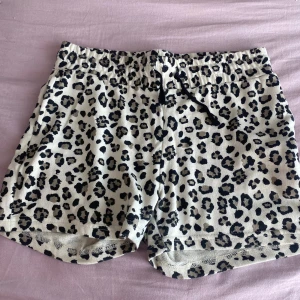 Leopardmönstrade shorts XOXO Friends - Snygga shorts från XOXO Friends med leopardmönster i svart och beige. De har elastisk midja med snörning och är tillverkade i mjuk bomull, perfekta för en chill sommarlook. Passformen är normal och de är superbekväma att ha på sig.