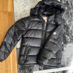 Svart Moncler Jacka - Säljer en snygg svart dunjacka från Moncler med glansig finish. Jackan är perfekt för kyliga dagar med stil och är dessutom i nyskick. Storlek 4 (L) NFC- Scan är fungerande! Kan tänka mig att gå ner i pris vid en snabb och smidig affär! Har du några frågor eller funderingar tveka inte på att höra av dig!