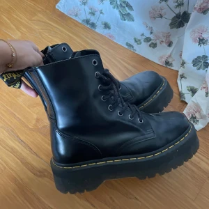 Dr. Martens Jadon boots svarta 38 - Säljer ett par svarta Dr. Martens Jadon boots i storlek 38. Skorna har grov plattformsula, snörning framtill, dragkedja på sidan och klassiska gula sömmar. Tillverkade i skinn och har rund tå. Perfekta för dig som vill ha en edgy och tidlös look.