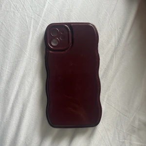 iPhone 11 Skal Vågformad Mörkröd - Vågformat skal i vinröd färg, anpassat för iPhone 11. Ger bra skydd mot repor och stötar. Skalet är i gott skick med mindre tecken på användning. Perfekt passform för kameran och knappar. Unik design som ger ett säkert grepp. (Jag betalar frakt)