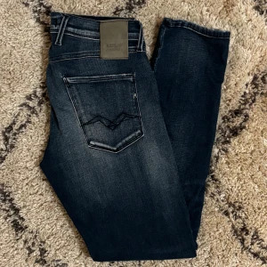 Replay Anbass mörkblå  - Snygga Replay Anbass jeans i mörkblå tvätt med slitningar och klassiska fem fickor. Slim fit-modell med låg till medelhög midja och tydliga kontrastsömmar. Jeansen har dragkedjegylf och är tillverkade i stretchig denim för extra komfort.