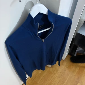 Marinblå merinoullströja Riley M - Snygg marinblå långärmad tröja från Riley i mjuk merinoull. Tröjan har en hög krage med half zip-dragkedja framtill och en stilren, klassisk look. Perfekt för dig som gillar enkel och clean stil med lite edge.
