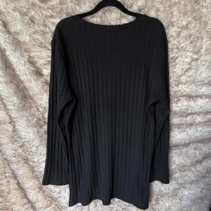 Svart ribbad långärmad tröja med slits - Svart långärmad tröja med ribbat mönster och rund halsringning. Hög slits på sidorna.  Tröjan har en loose passform och är tillverkad i ett mjukt, stretchigt material. 