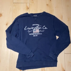 Mörkblå Lexington sweatshirt - Mörkblå sweatshirt från Lexington med broderad logga och amerikansk flagga framtill. Tröjan har rund halsringning, långa ärmar och ribbade muddar. Perfekt för en avslappnad och stilren look.