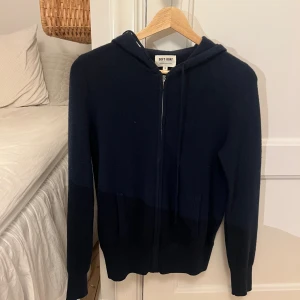 Mörkblå hoodie i kashmir från Soft Goat - Mysig mörkblå hoodie från Soft Goat i 100% kashmir. Tröjan har dragkedja framtill, huva med snörning och två fickor. Långärmad och super snygg!!