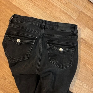 Svarta bootcut jeans Lager157 - Svarta jeans från 157 i bootcut-modell med snygga fickor bak med lock och silverfärgade knappar. Klassisk femficksdesign och normalhög midja. Jeansen är i stretchigt bomullsmaterial och passar perfekt till dig som gillar en tidlös look.