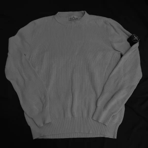 Grå ribbad tröja från Stone Island - Säljer en snygg vit ribbad tröja från Stone Island. Perfekt för höst och vinter, och den ikoniska loggan på ärmen ger en extra touch av stil. Passar både till vardags och lite finare tillfällen. Om du har några frågor är det bara att skriva. Kan bytas också 